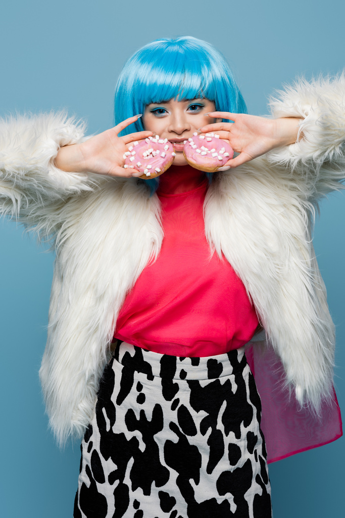 Uśmiechnięta Azjatka w stylu pop art trzymająca pączki odizolowane na niebiesko  - Zdjęcie, obraz