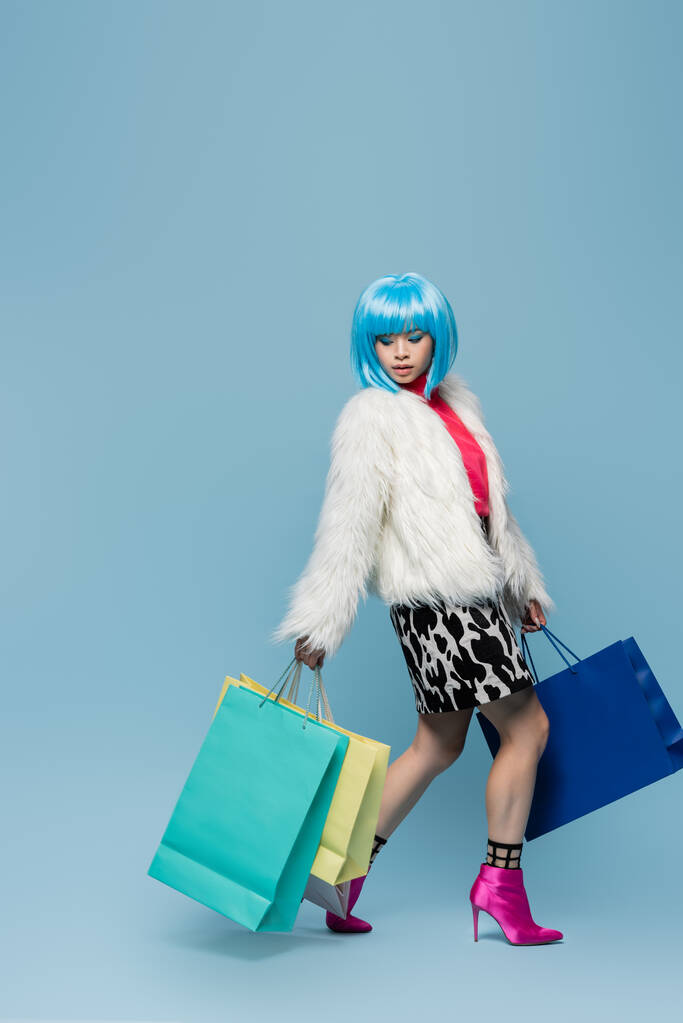 Stylish asian woman in pop art style holding shopping bags on blue background  - Photo, Image