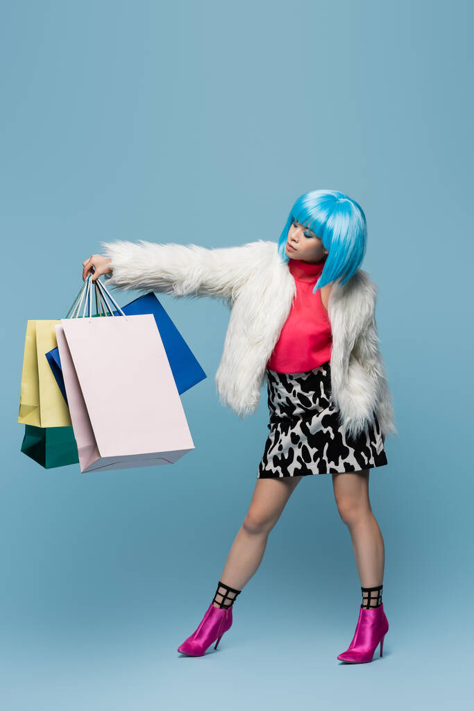 Mooie aziatische vrouw in pop art stijl op zoek naar winkeltassen op blauwe achtergrond  - Foto, afbeelding