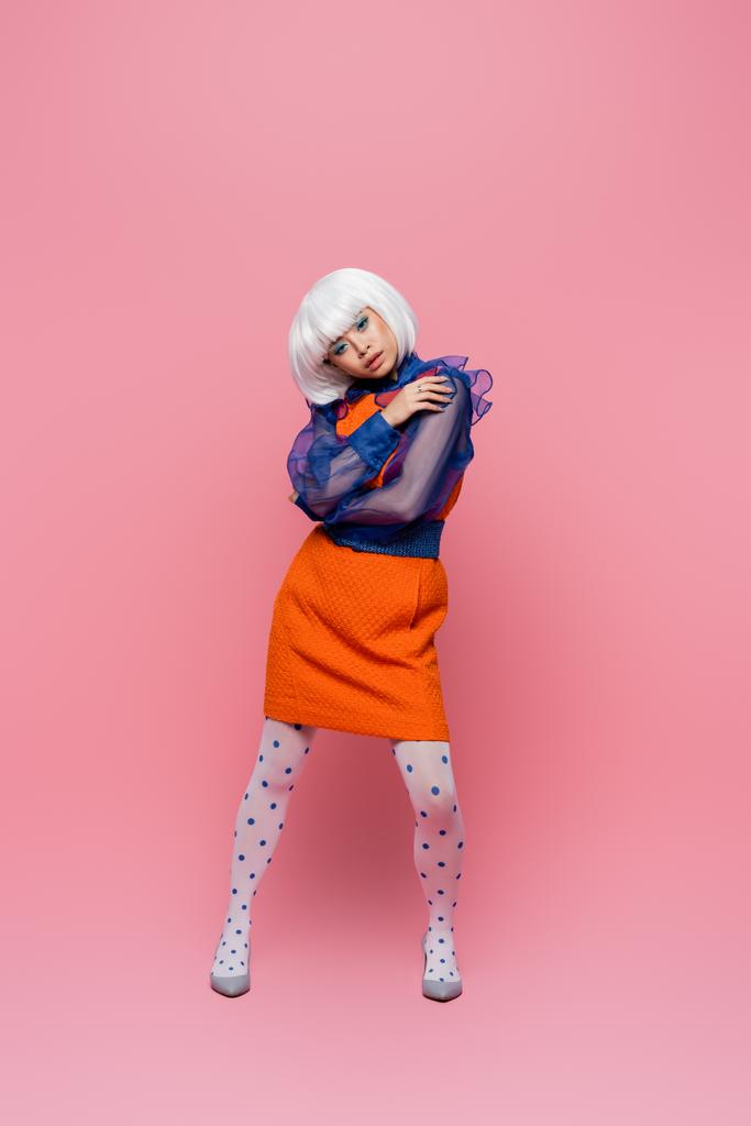 Stylish asian woman in heels and white wig posing on pink background  - Photo, Image