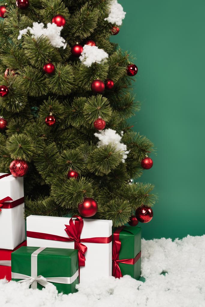 Geschenke in der Nähe von Weihnachtsbaum und dekorativem Schnee auf grünem Hintergrund  - Foto, Bild