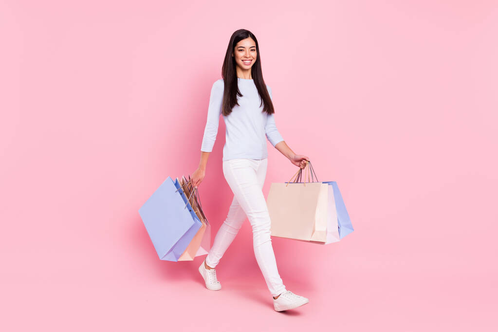 Вид в полный рост на привлекательную худенькую жизнерадостную девушку с сумками подарков на розовом цветовом фоне - Фото, изображение