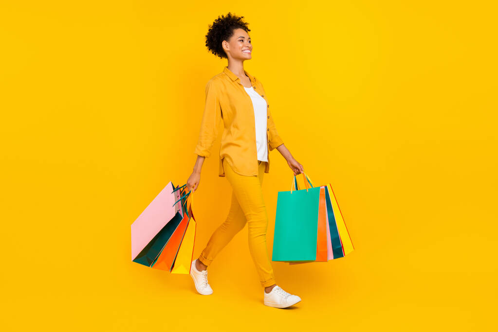 Longitud completa cuerpo tamaño foto mujer caminar con paquetes a la venta aislado vívido color amarillo fondo - Foto, imagen