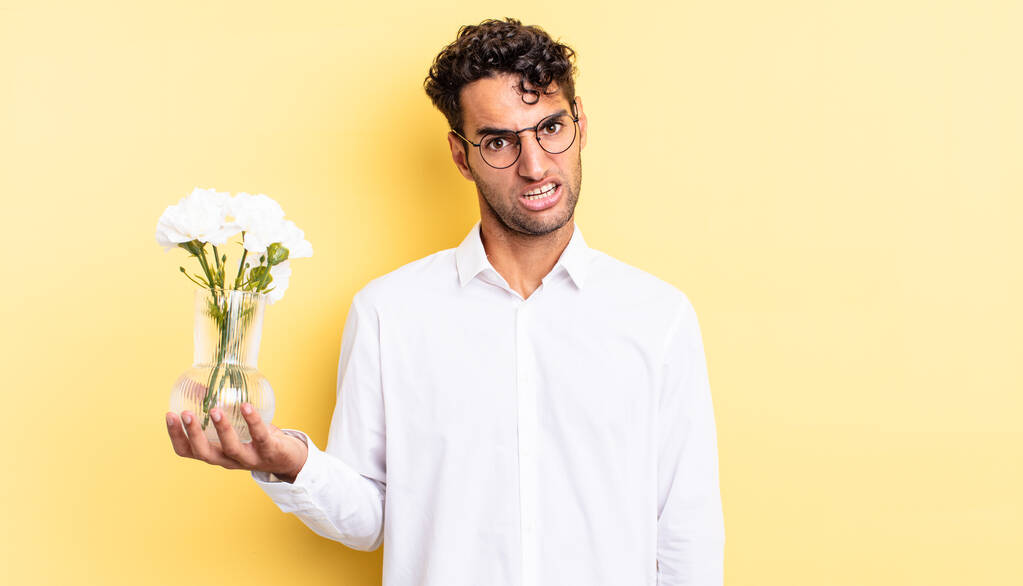 hombre guapo hispano sintiéndose perplejo y confundido. concepto de maceta flores - Foto, Imagen