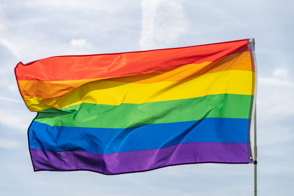 Szivárvány zászló (LMBT mozgalom) a napfényes kék égbolt hátterében. Színes meleg zászló lengetése. - Fotó, kép