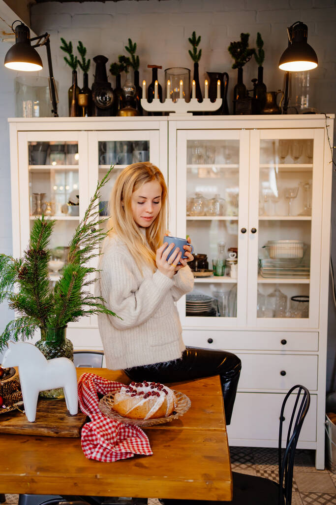 Красивая блондинка пьет чай на кухне, украшенной к Новому году. - Фото, изображение