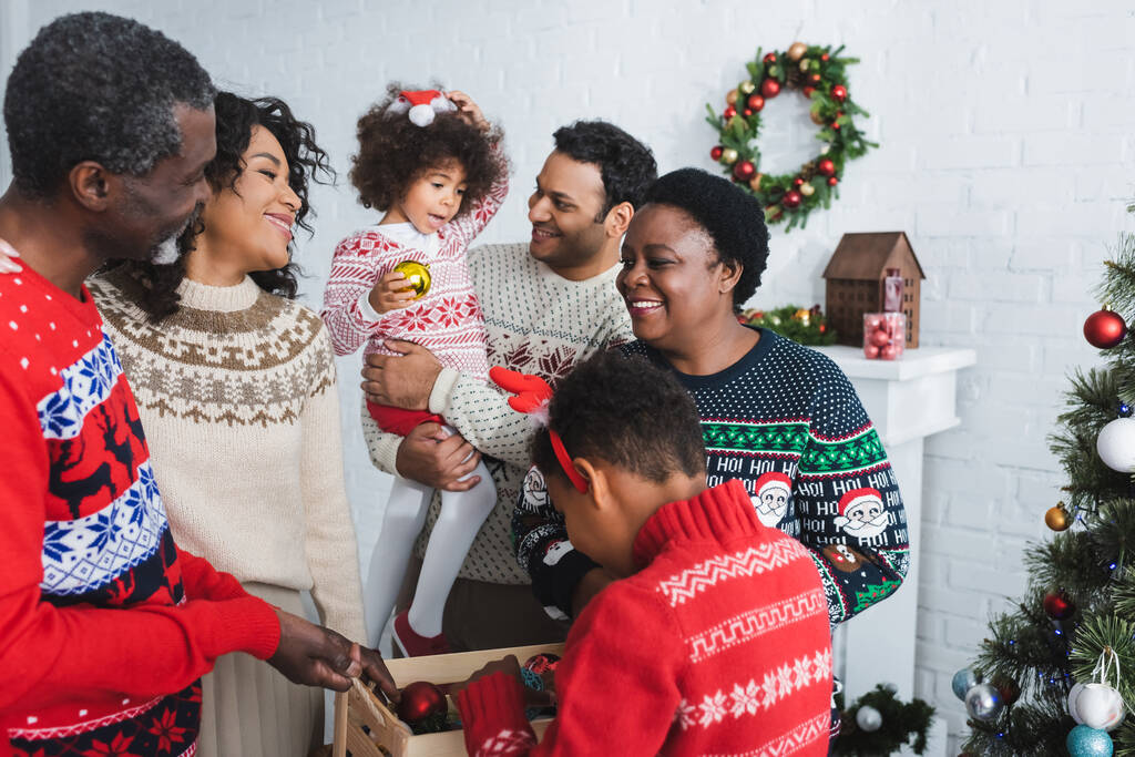 fiú gazdaság fa doboz karácsonyi labdák közelében vidám afro-amerikai család a nappaliban - Fotó, kép