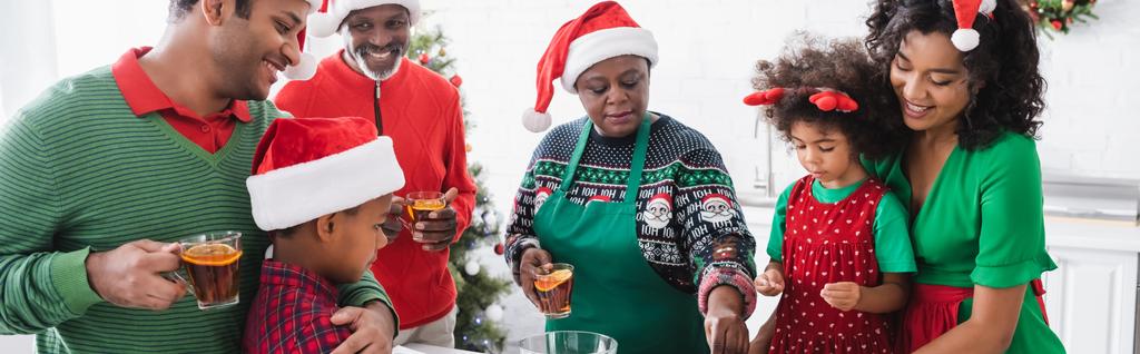 サンタ・ハットのアフリカ系アメリカ人の家族はキッチンのおばあちゃん料理の近くで笑っています - 写真・画像