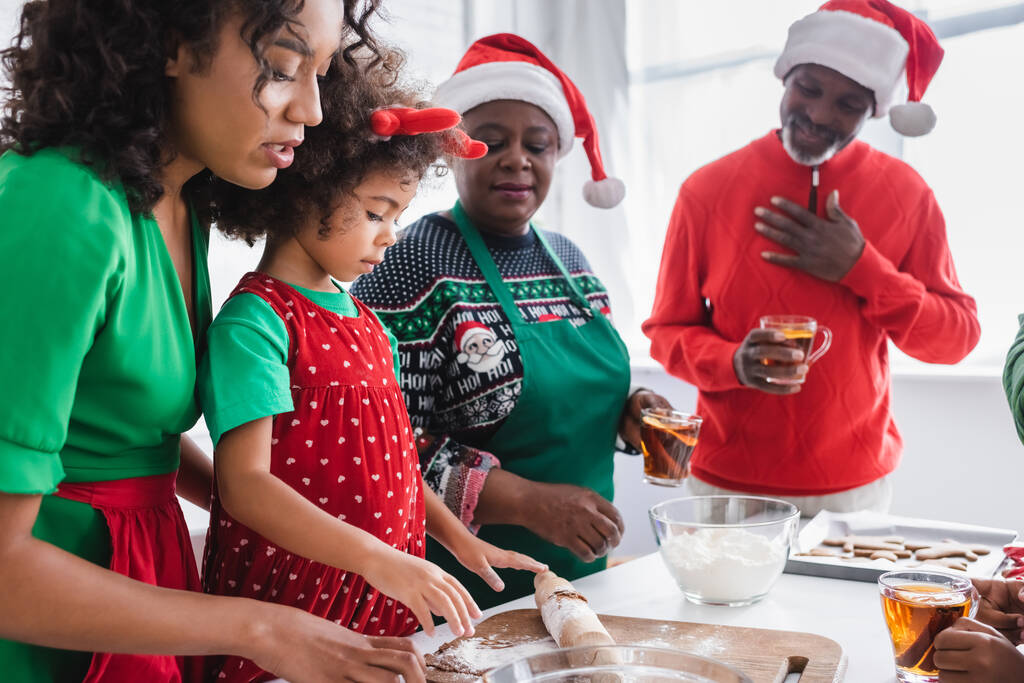 blij Afrikaans amerikaanse grootouders op zoek naar kleindochter bereiden kerstkoekjes met moeder - Foto, afbeelding