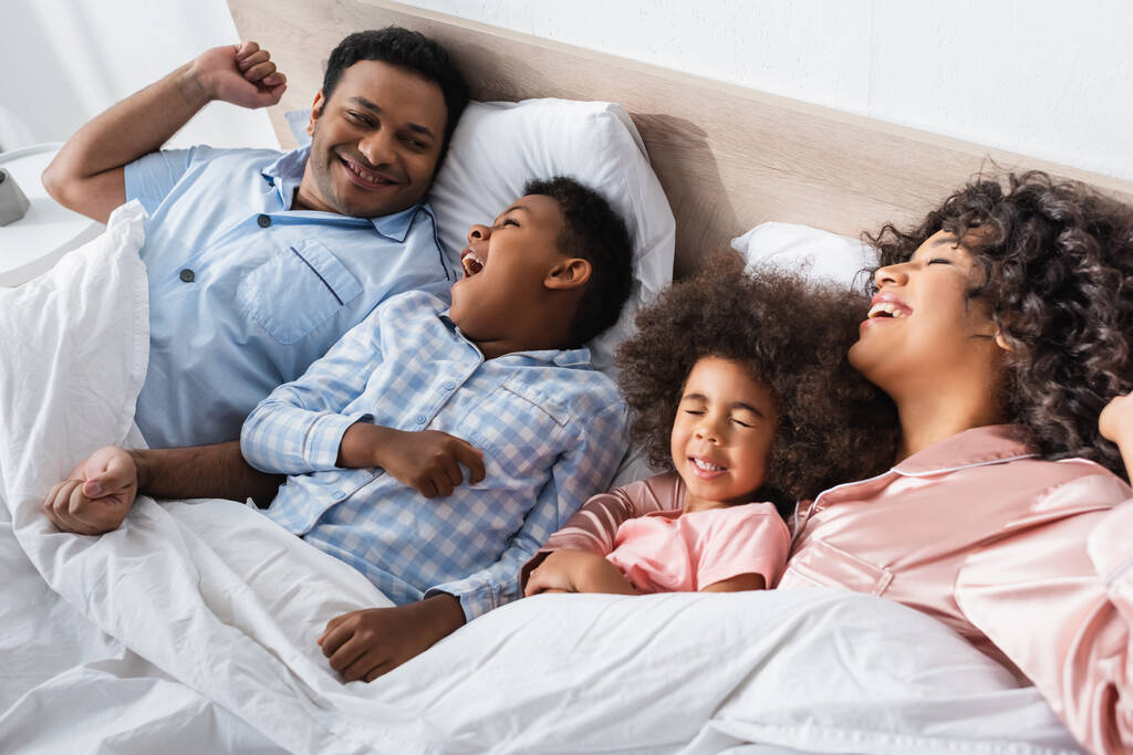 афроамериканський хлопчик позіхання вранці, лежачи в ліжку біля щасливих батьків і сестри
 - Фото, зображення