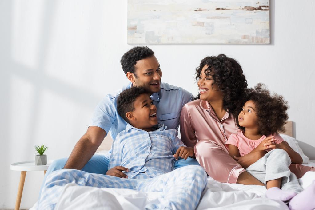 glückliches afrikanisch-amerikanisches Paar spricht im Bett neben fröhlichen Kindern - Foto, Bild