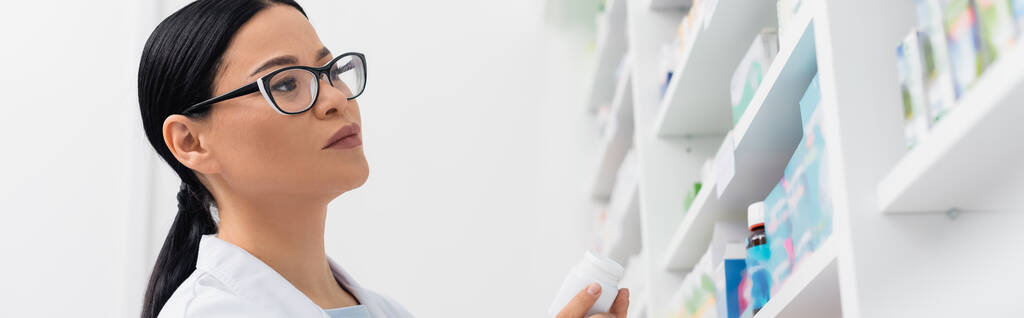 farmacéutico asiático en gafas mirando la medicación en farmacia, bandera - Foto, imagen