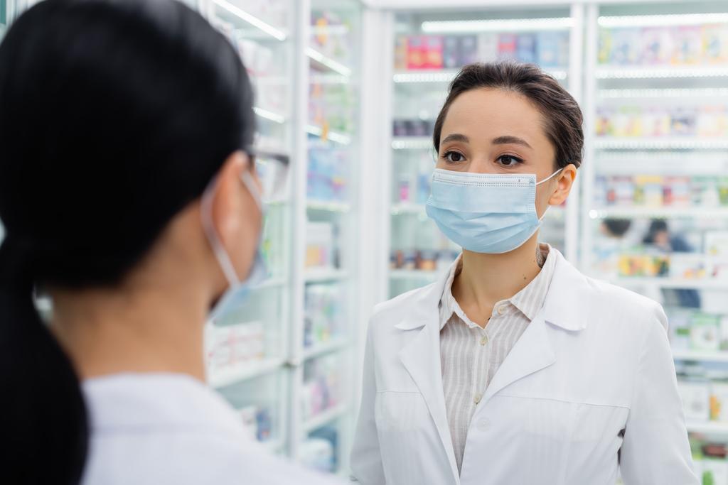 wytatuowany farmaceuta w masce medycznej patrzący na rozmazanego kolegę - Zdjęcie, obraz