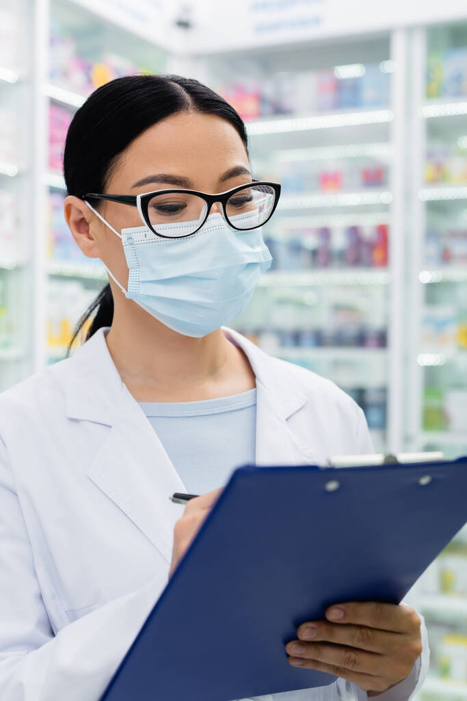 азіатський фармацевт в окулярах і медична маска тримає розмиті кишені
  - Фото, зображення