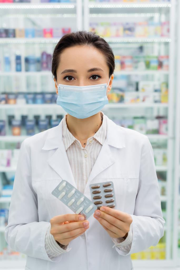 аптекарь в медицинской маске держит пузыри пакеты с лекарствами  - Фото, изображение