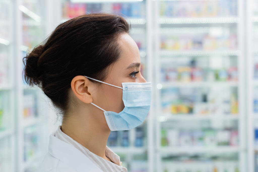 widok z boku brunetka aptekarz w medycznym maski  - Zdjęcie, obraz