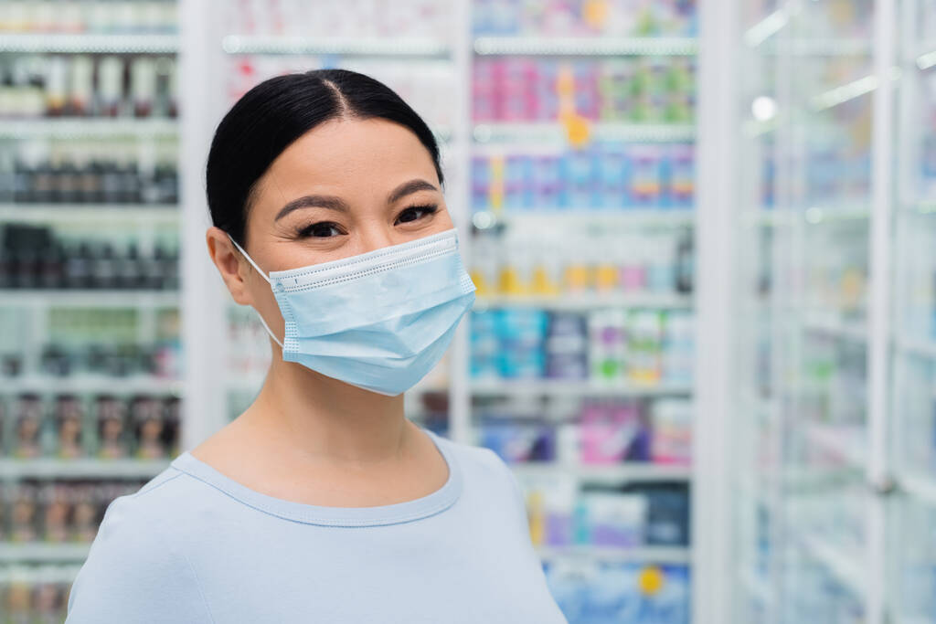 asiático cliente en médico máscara mirando en cámara en droguería - Foto, Imagen