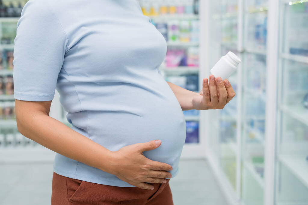 vista cortada de garrafa cliente grávida segurando com vitaminas na farmácia - Foto, Imagem