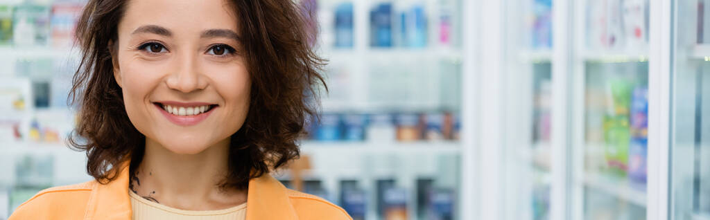 Ευτυχισμένη και με τατουάζ γυναίκα χαμογελά στο φαρμακείο, πανό - Φωτογραφία, εικόνα