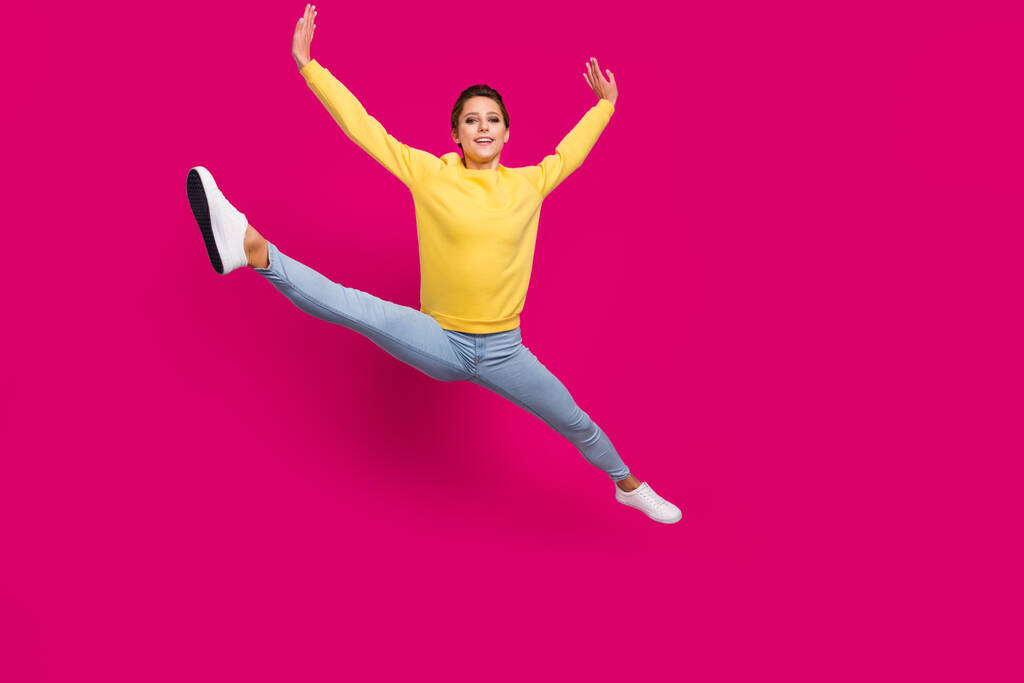 Фото чарівної солодкої молодої жінки, одягненої в жовтий пуловер, стрибає, розтягуючись посміхаючись, ізольований рожевий колір фону
 - Фото, зображення