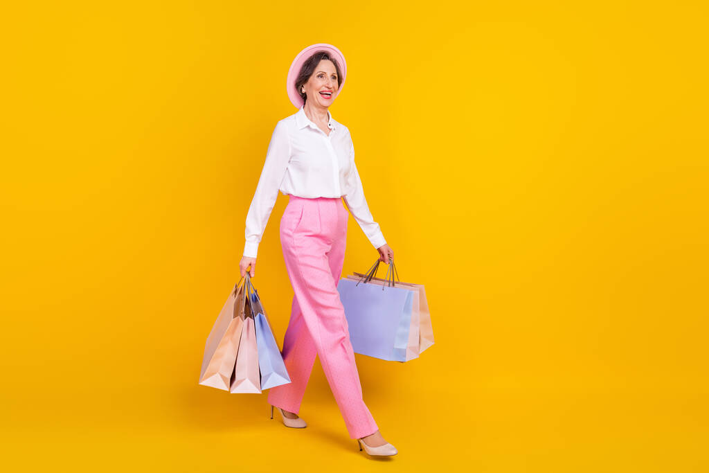 Full body profil boczny zdjęcie starszej kobiety szczęśliwy pozytywny uśmiech iść spacer trzymać torby zakupy izolowane na żółtym tle koloru - Zdjęcie, obraz