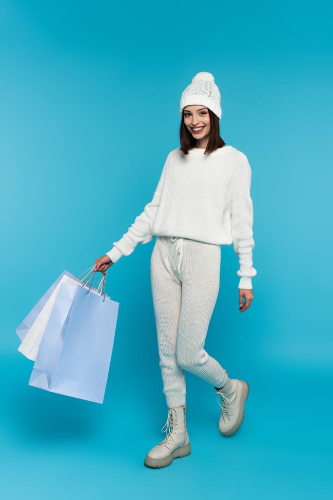 Mavi arka planda yürüyen alışveriş çantalı olumlu bir kadın.  - Fotoğraf, Görsel