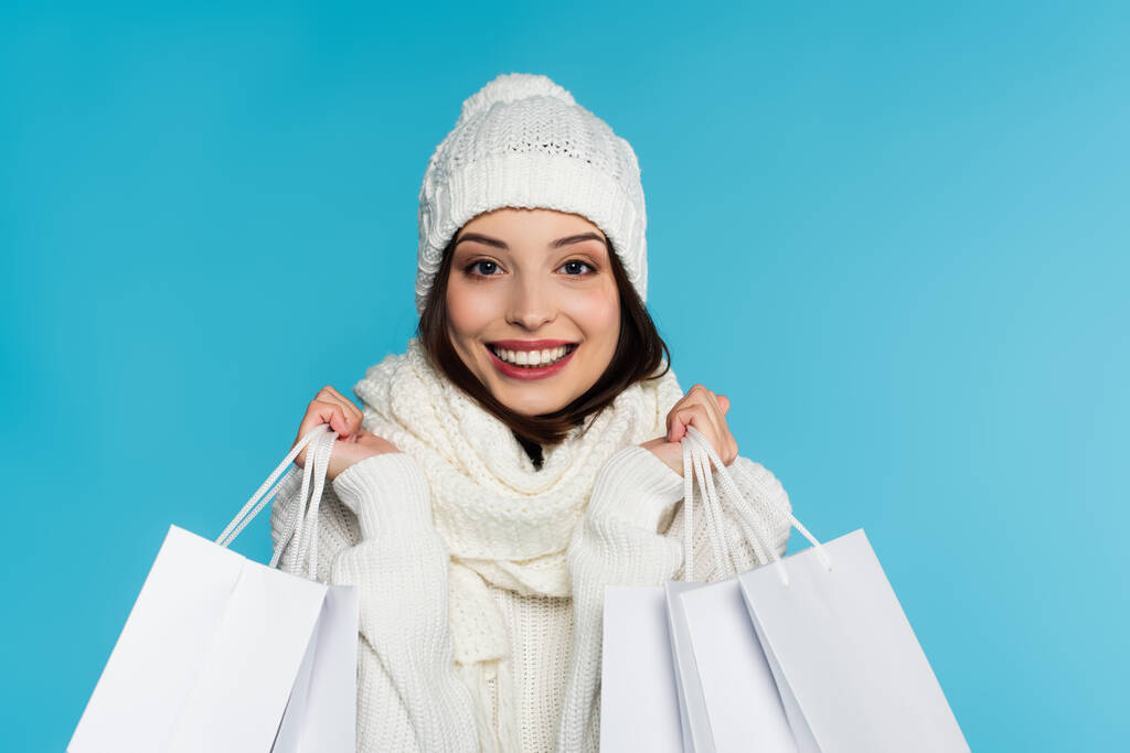 Onnellinen nuori nainen valkoinen hattu ja huivi tilalla ostoskassit eristetty sininen  - Valokuva, kuva