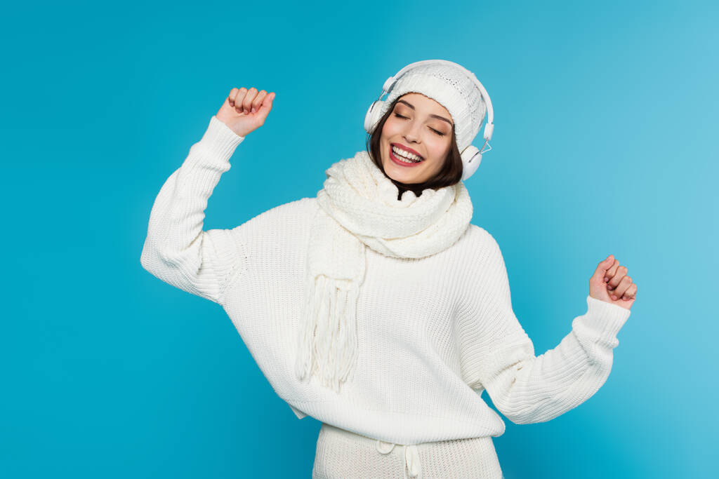 Happy woman in warm clothes and headphones dancing isolated on blue  - Photo, Image
