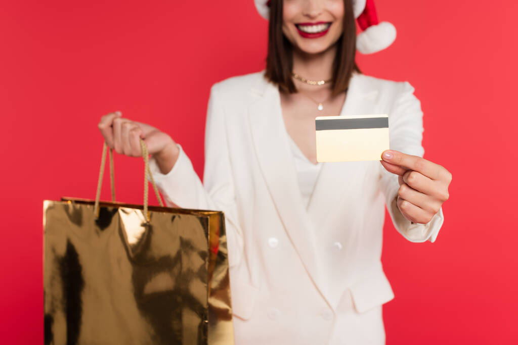 Noel Baba şapkalı bulanık kadın elinde alışveriş çantası ve kredi kartıyla kırmızı ışıkta izole edilmiş.  - Fotoğraf, Görsel