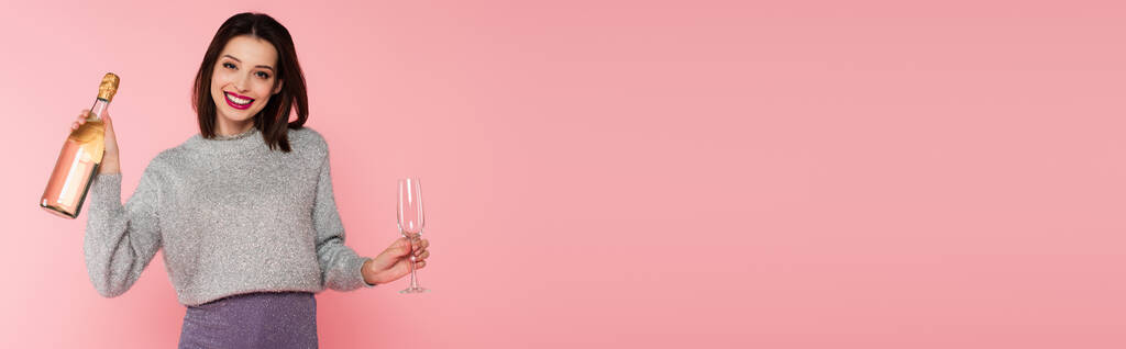 Donna positiva in possesso di bottiglia di champagne e vetro isolato su rosa, banner  - Foto, immagini