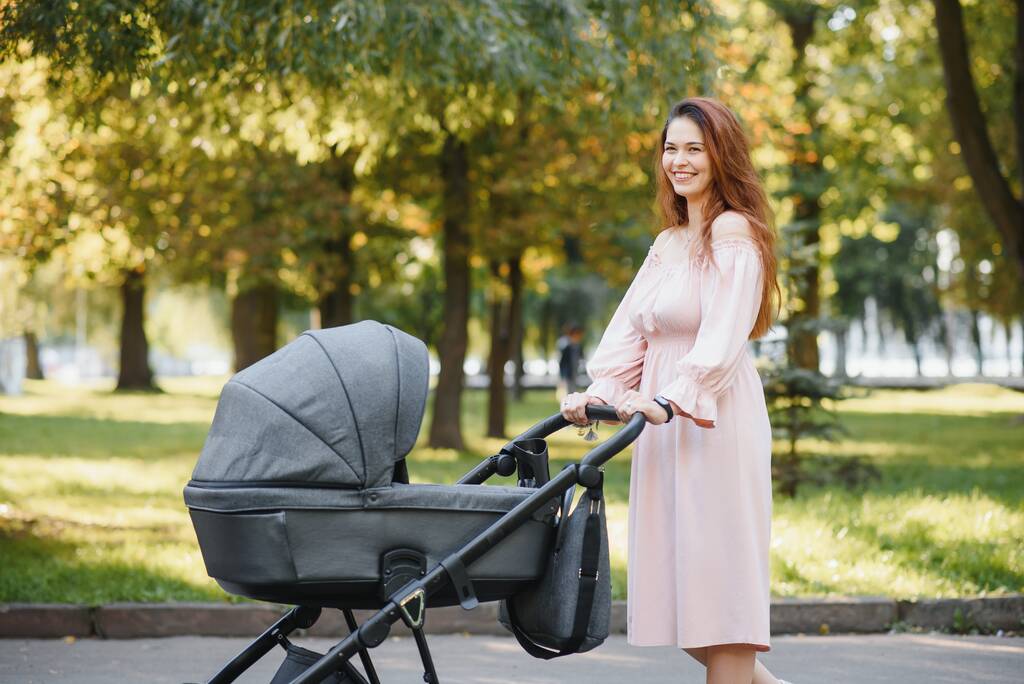 concept de famille, d'enfant et de parentalité - mère heureuse marchant avec une poussette pour bébé dans le parc
. - Photo, image