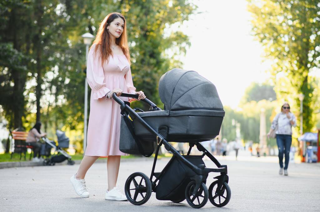 familie-, kinder- en ouderschap concept - gelukkige moeder wandelen met baby wandelwagen in park. - Foto, afbeelding