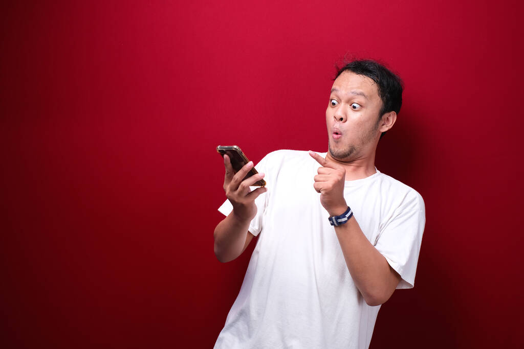 Jeune homme asiatique choqué quand il regarde et pointant smartphone - Photo, image