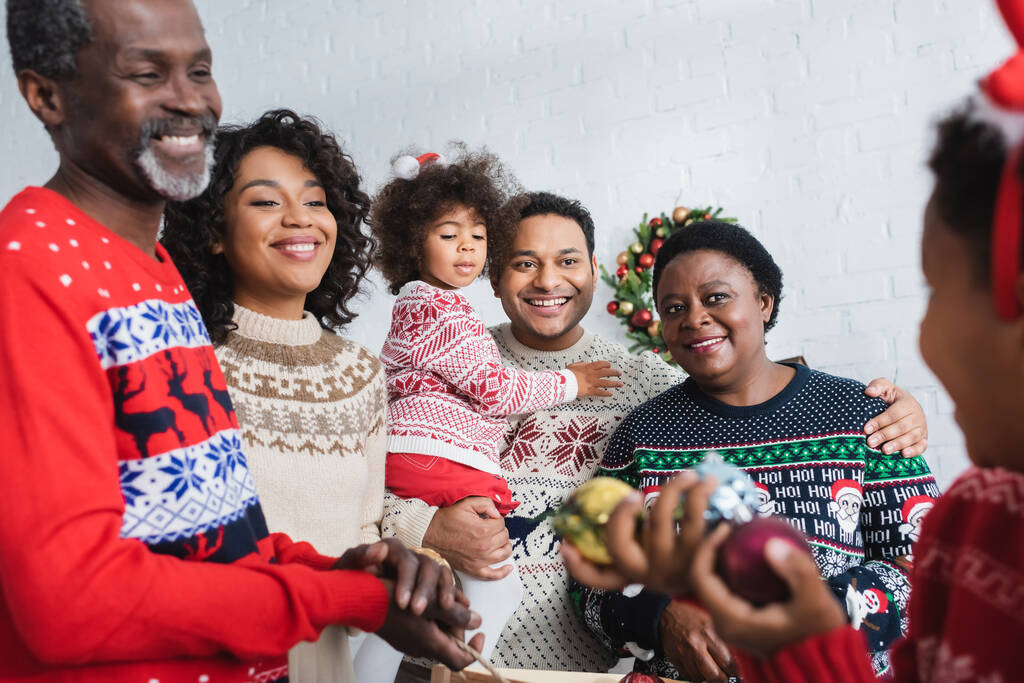 joyful african american family looking at blurred boy holding christmas balls - Photo, Image