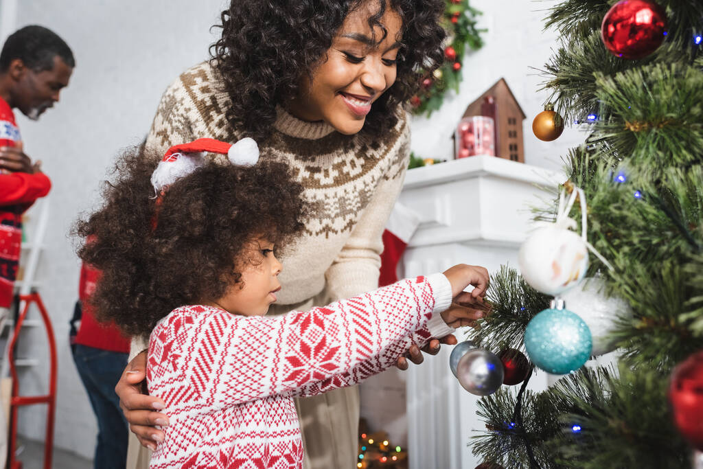 afro-américaine fille en santa chapeau décoration arbre de Noël près de maman heureuse - Photo, image