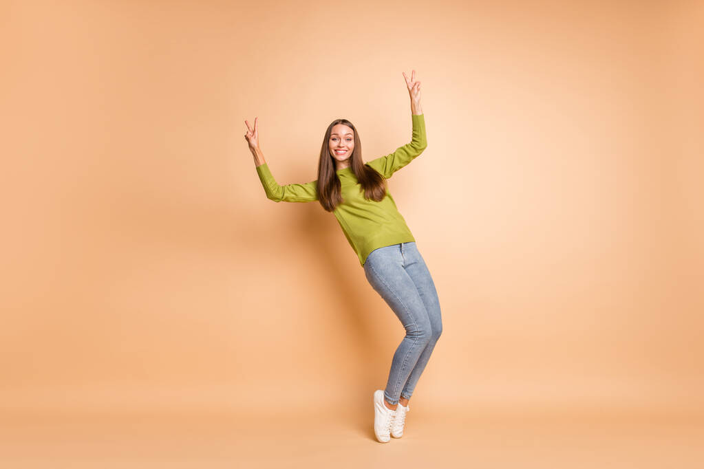 Foto de longitud completa de señora puntillas muestran dos v-signos de desgaste verde jersey calzado jeans aislados de color beige fondo - Foto, imagen