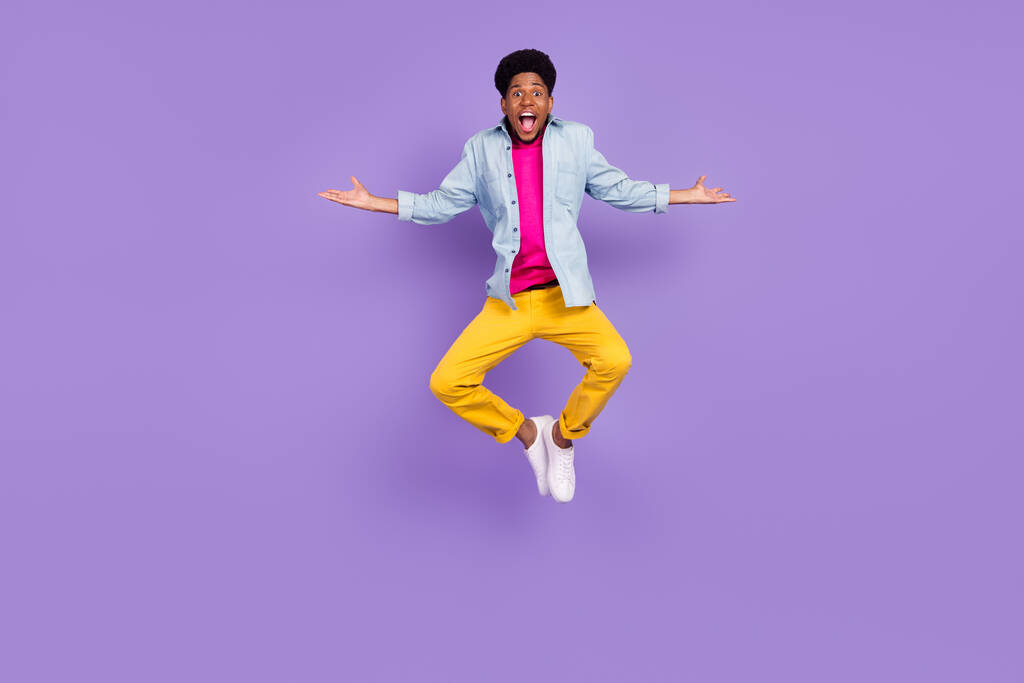 Foto van zorgeloze grappige man springen verhogen handen weekend vrije tijd dragen blauw shirt geïsoleerde paarse kleur achtergrond - Foto, afbeelding
