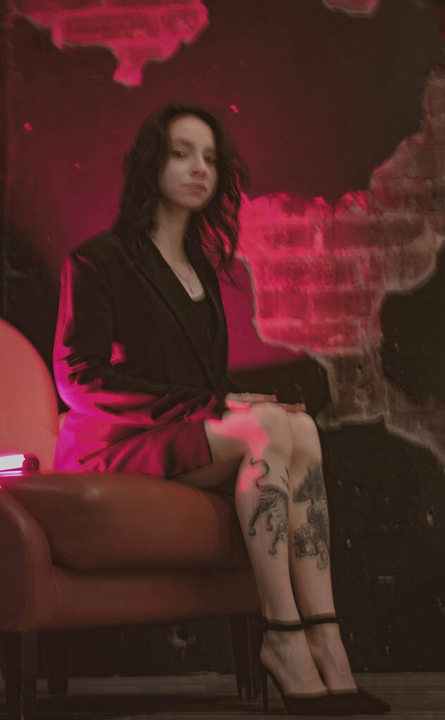 menina com tatuagens em uma jaqueta e sapatos sexy em néon vermelho - Foto, Imagem