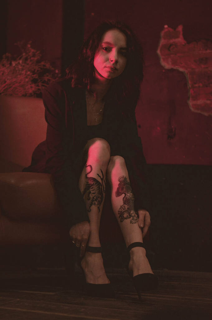 girl with tattoos in a jacket and sexy shoes in red neon - Photo, Image