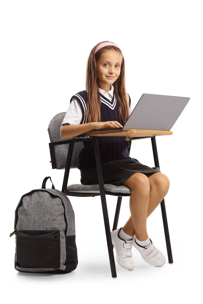 Colegiala sentada en una silla de clase y usando una computadora portátil aislada sobre fondo blanco - Foto, Imagen