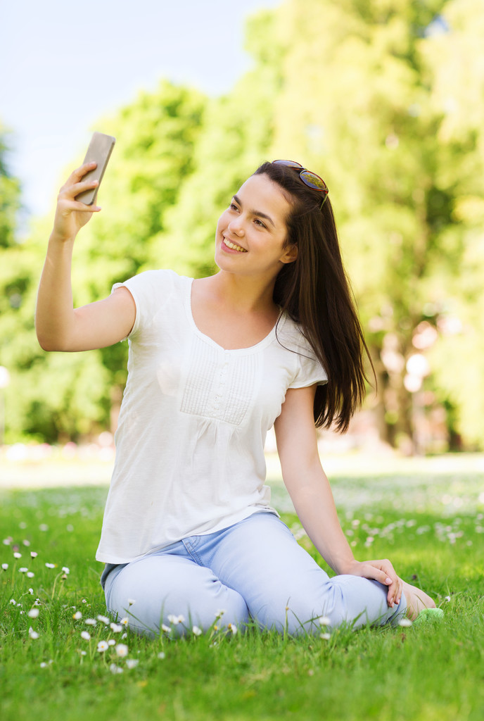усміхнена молода дівчина зі смартфоном сидить у парку
 - Фото, зображення