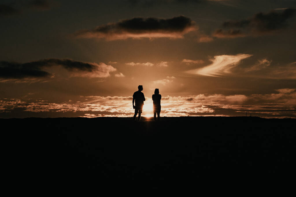 Die Silhouetten eines romantischen Paares, das die schöne Aussicht auf den Sonnenuntergang bewundert - Foto, Bild