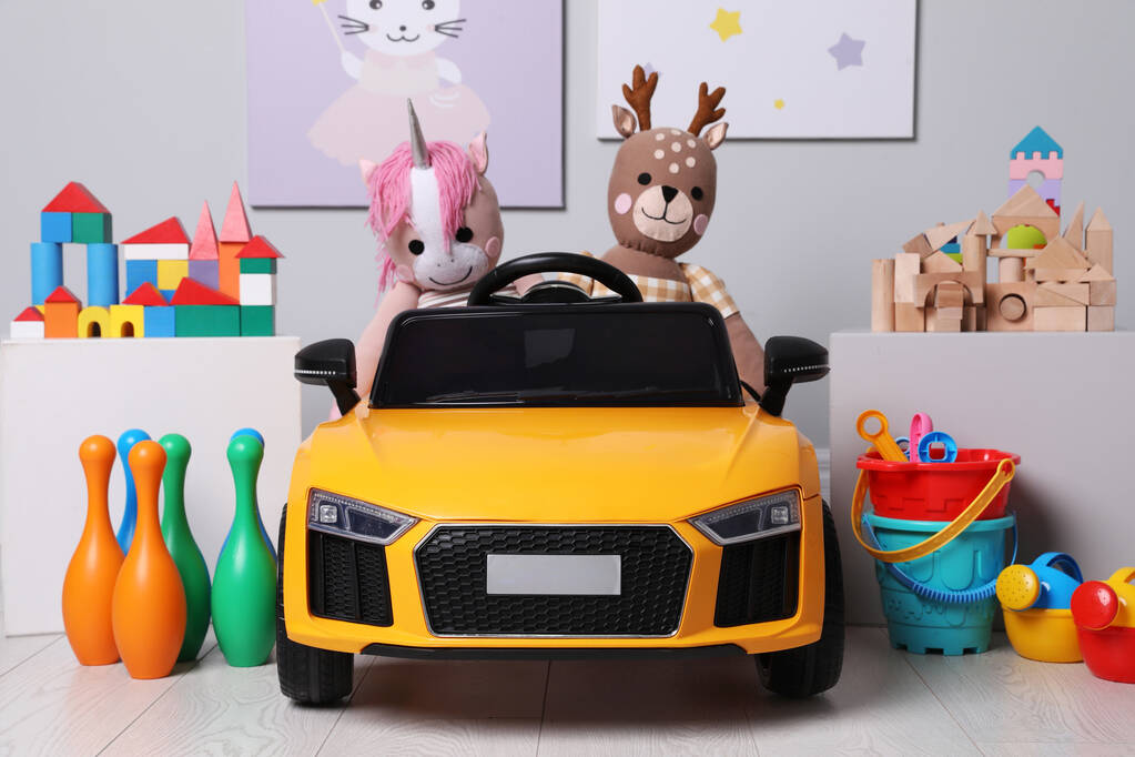 Дитячий електричний автомобіль з іншими іграшками біля світлої стіни в ігровій кімнаті
 - Фото, зображення