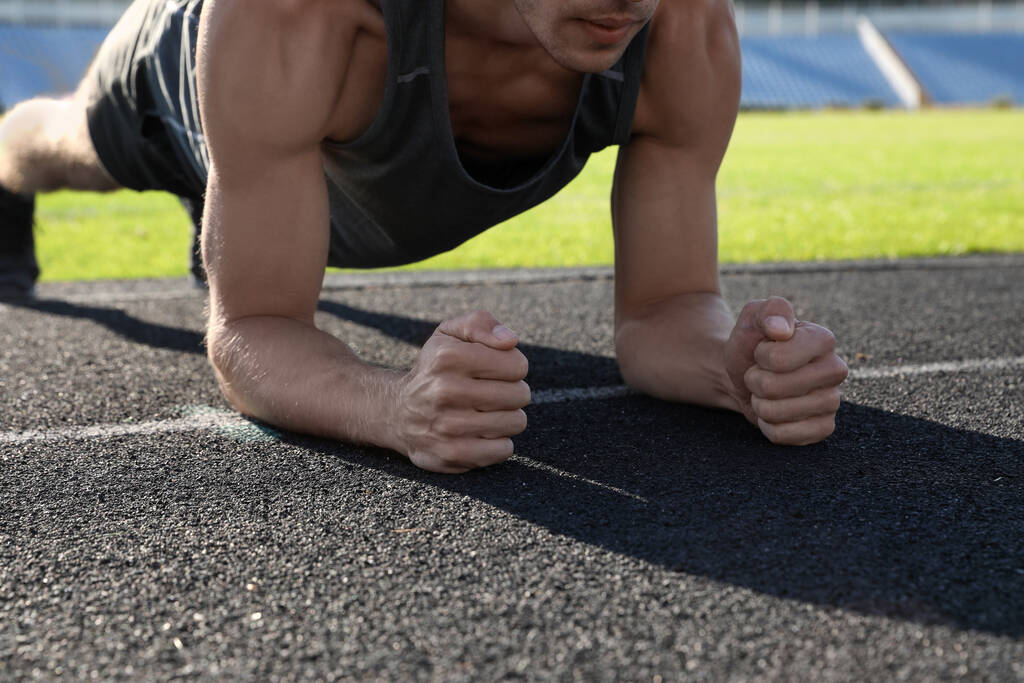 Sportieve man doet plank oefening in het stadion, close-up - Foto, afbeelding