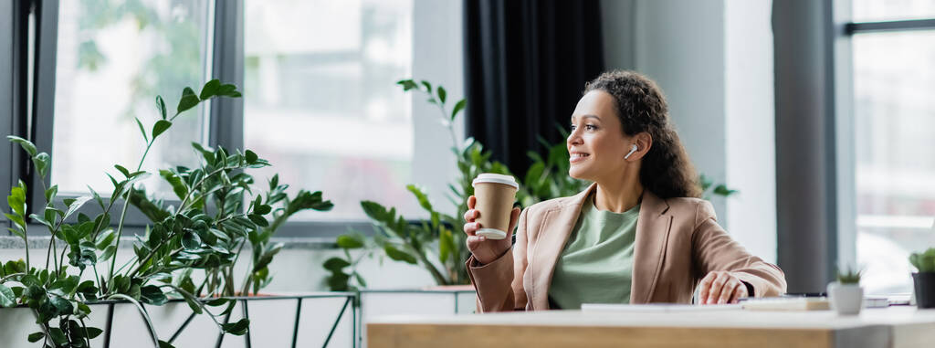 gelukkige Afro-Amerikaanse zakenvrouw luisteren muziek tijdens koffiepauze op het werk in het kantoor, banner - Foto, afbeelding