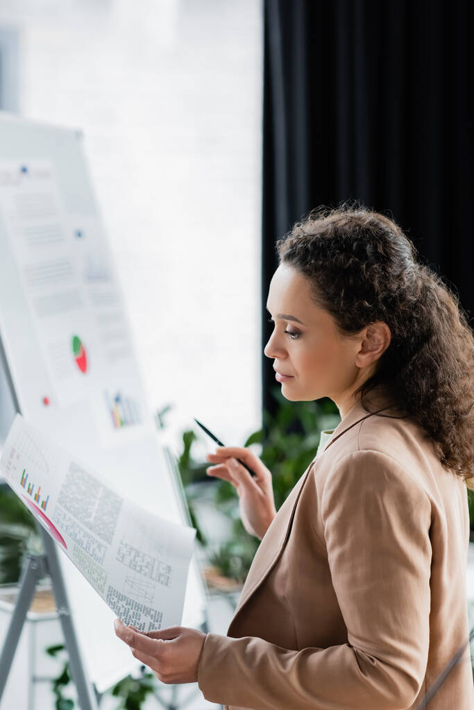Африканская американская бизнесвумен смотрит на инфографику во время работы в офисе - Фото, изображение