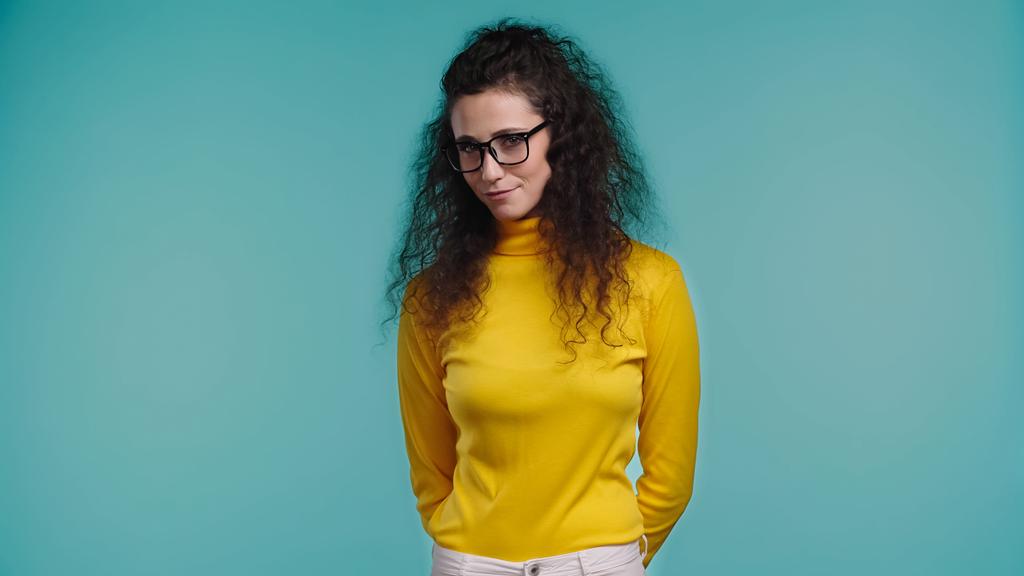 stydlivá mladá žena v brýlích stojící izolované na modré  - Fotografie, Obrázek