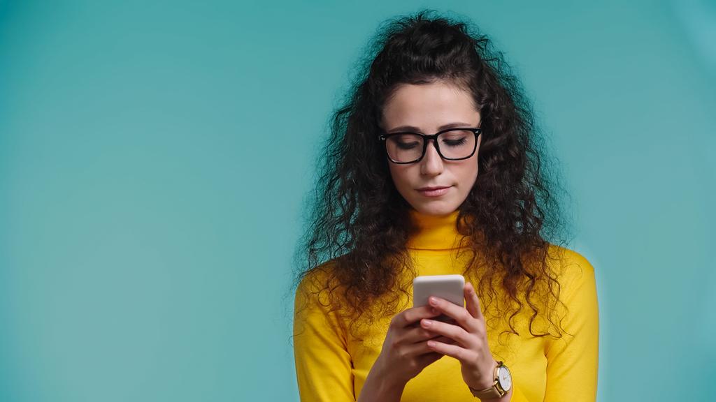 νεαρή γυναίκα σε γυαλιά μηνυμάτων στο smartphone απομονώνονται σε μπλε  - Φωτογραφία, εικόνα