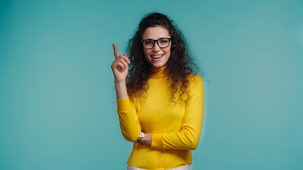 Ευτυχισμένη νεαρή γυναίκα με γυαλιά έχοντας την ιδέα απομονωμένη στο μπλε - Φωτογραφία, εικόνα