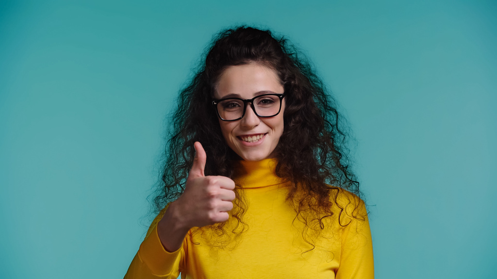 šťastná žena v brýlích a roláku ukazující palec nahoru izolované na modré - Fotografie, Obrázek